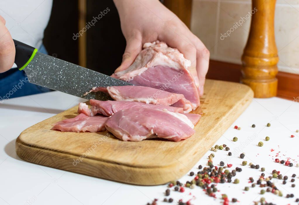 Slicing fresh meat with a knife on a kitchen board and pepper