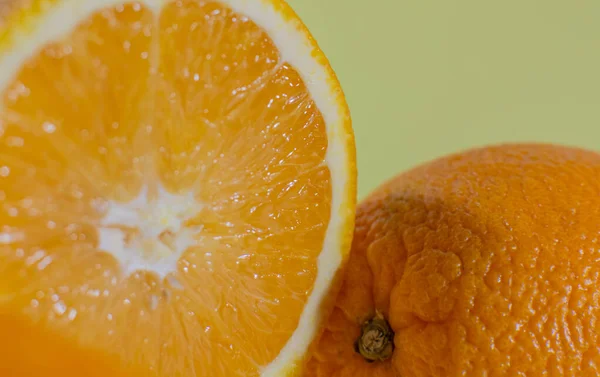 Половина оранжевого рядом с целым апельсином на зеленом фоне — стоковое фото