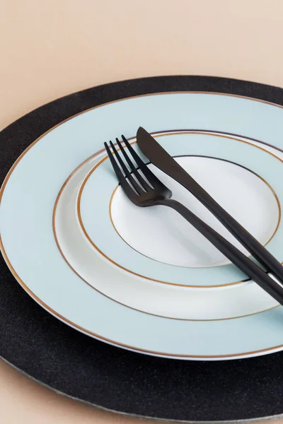 Table set with empty serving plate with fork and knife on it at beige background. Serving plate with black silverware