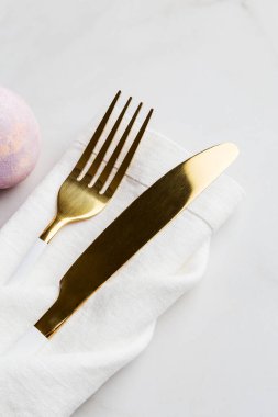 Çatal ve bıçağı paskalya yumurtasıyla kapat. Beyaz peçeteli altın çatal bıçak takımı ve beyaz arka planda pembe Paskalya yumurtası. Restoran için Paskalya menüsü kavramı