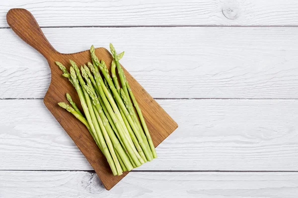 Asparagus on cutting board at white wood background. Top view, flat lay, lay out, copy space for text.