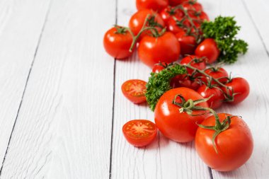 Arkaplan olarak beyaz tahta üzerinde yeşil maydanozlu farklı taze kırmızı domatesler. Sağlıklı İtalyan yemekleri için içerikli fotokopi alanı resmi kavramı