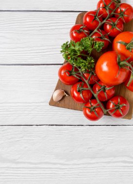 Tahta üzerinde kırmızı taze domates maydanozlu tahta ve beyaz ahşap arka planda sarımsak.