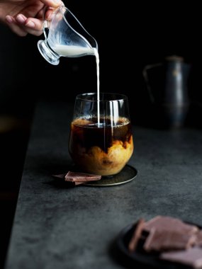 Koyu arkaplanda sütlü kahve. Soğuk kahveye el kreması döküyorum. Lezzetli bir içecek ve kahve kavramı. Metin, menü veya tarif için boşluk kopyala