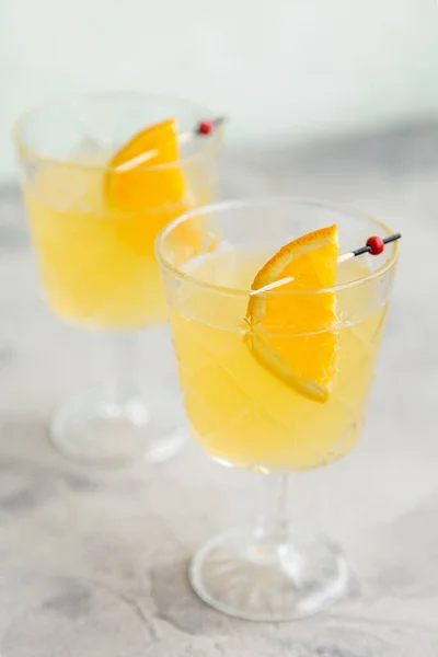 Glass with orange lemonade with slice of orange at toothpicks at bright white background. Concept of fresh cool beverages