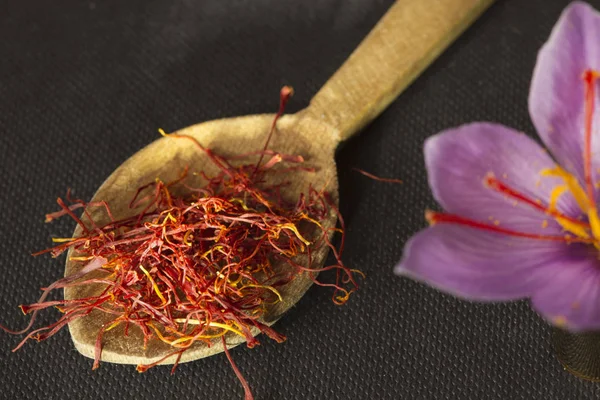 Tipos de açafrão em uma colher e flor de açafrão em um backgroun preto — Fotografia de Stock