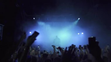 Duman içinde sahnede mikrofonlu bir şarkıcı. Sahnenin etrafında telefonla gezen hayranlar