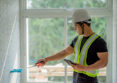 Beyaz kask takan güçlü bir ustabaşı, şantiyede telsiz mesajı ve tablet tutuyor..