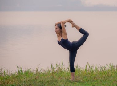 Güçlü kadınlar göl kenarında zor yoga hareketleri yaparlar..