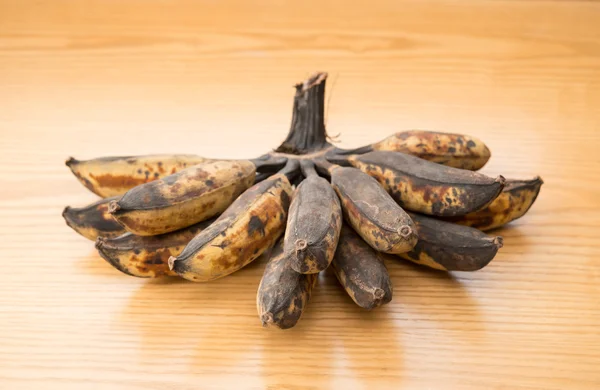 Monte de bananas pretas sobreamadurecidas em um fundo de madeira — Fotografia de Stock