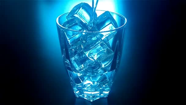 Pouring glass of water with ice cubes with blue backlit in slow motion at 120fps in dark — Stockvideo