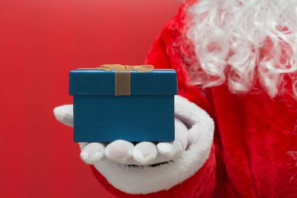 Santa Claus entrega una caja de regalo de Navidad sobre fondo rojo — Foto de Stock