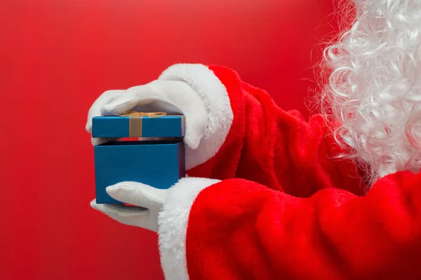 Santa Claus sosteniendo la mano Caja de regalo de Navidad sobre fondo rojo — Foto de Stock