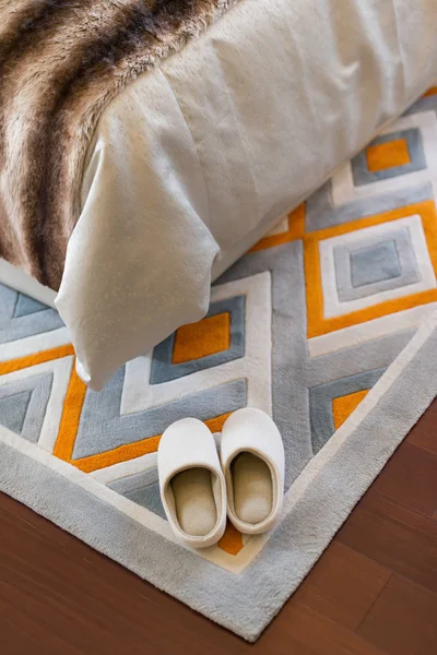 Paar witte slippers op tapijt in de buurt van een bed — Stockfoto