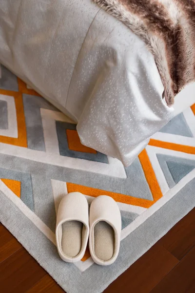 Paar witte slippers op tapijt in de buurt van een bed — Stockfoto