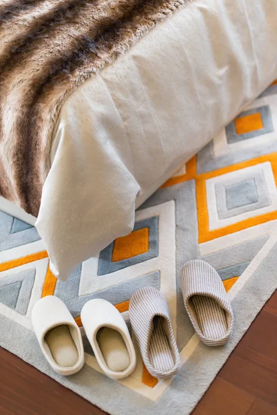 Twee paar witte slippers op tapijt in de buurt van een bed — Stockfoto