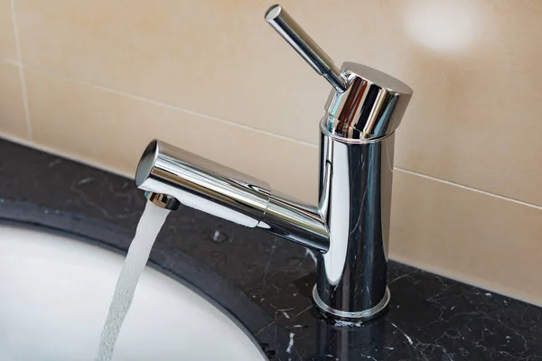 Water loopt uit van roestvrij staal kraan tot een wastafel in badkamer — Stockfoto