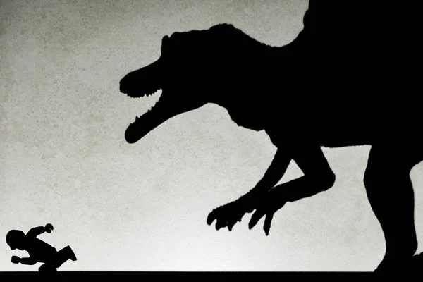 Spot light projection shadow of a spinosaurus toy chasing a running human — Stock Photo, Image