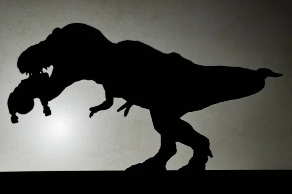 Тень тираннозавра, кусающего тело на стене без логотипа или торговой марки — стоковое фото