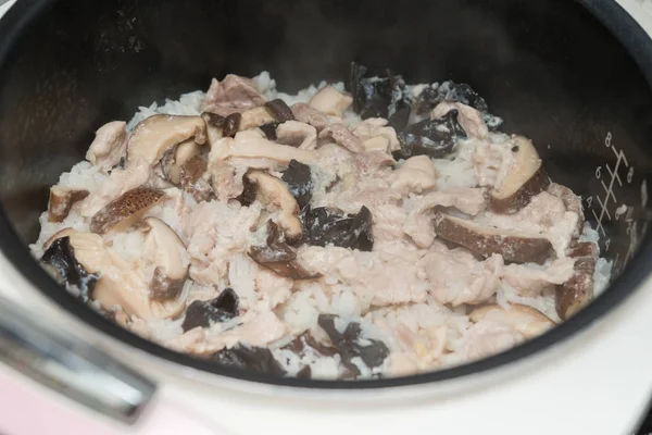 Приготовление риса со свиным грибом и черным грибом на электрической рисоварке дома — стоковое фото
