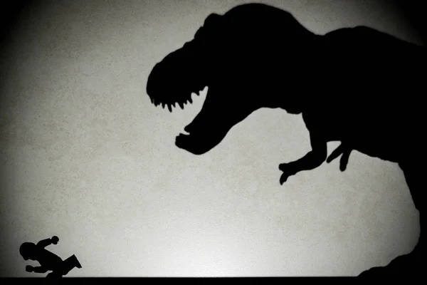 Cień tyranozaura goni człowieka na ścianie, nie logo lub znaków towarowych — Zdjęcie stockowe