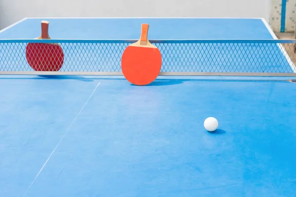 Raquetes de pingpong e bola e rede em uma mesa de pingpong azul — Fotografia de Stock