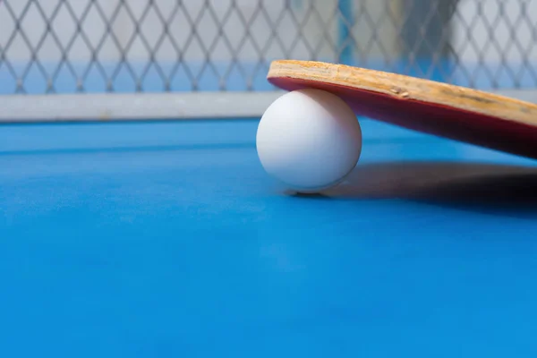 Raquetas de pingpong y bola y red en una mesa de pingpong azul de cerca — Foto de Stock
