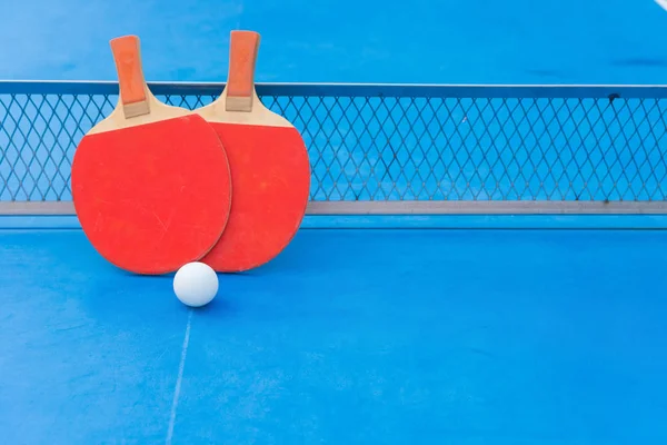 Dos raquetas de pingpong y bola y red en una mesa de pingpong azul con espacio para copiar — Foto de Stock