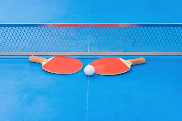 Raquetas de pingpong y pelota y red sobre una mesa de pingpong azul —  Fotos de Stock