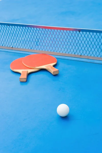 Raquetes de pingpong e bola e rede em uma mesa de pingpong azul — Fotografia de Stock