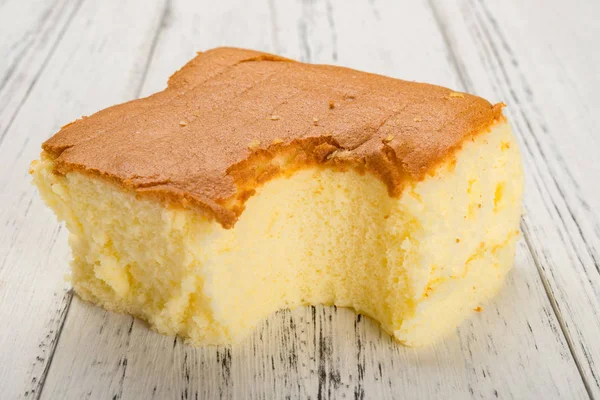 Gâteau éponge sur fond de bois blanc avec une morsure — Photo