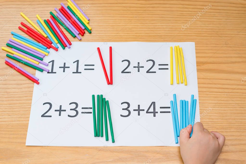 kid learning simple addition by counting numbers of sticks