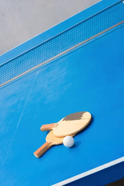 Viejas raquetas de pingpong y pelota y red sobre una mesa de pingpong azul —  Fotos de Stock
