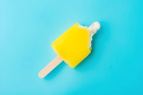 Bovenaanzicht gele popsicle met op een blauwe achtergrond bijt — Stockfoto