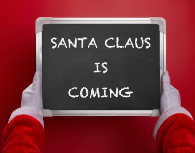 Claus Santa Noel Baba ile geliyor kırmızı zemin üzerine yazılmış bir siyah tebeşir tahtası tutan ilk kişi açılı görünüş