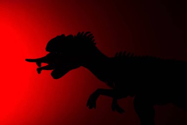 Karanlıkta kırmızı ışık ile daha küçük bir dinozor ısırma allosaurus gölgesi