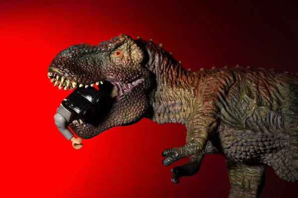 tyrannosaurus biting a small dinosaur with spot light on the head and red light on background