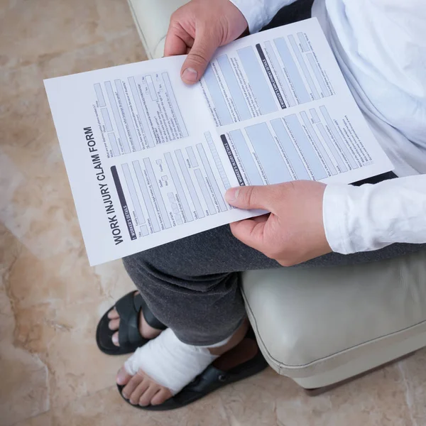 Man Wrapped Foot Sitting Sofa Reading Work Injury Claim Form — Stock Photo, Image