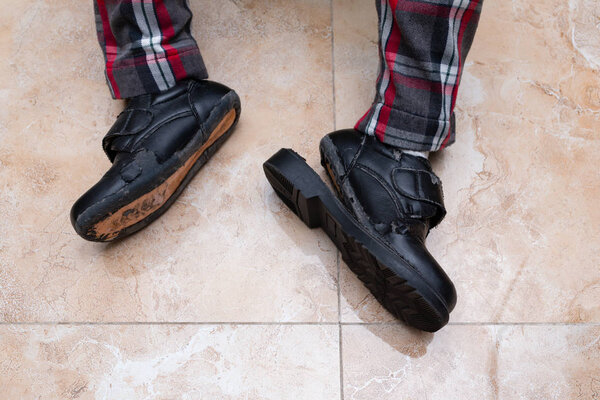 kid wearing a pair of badly worn out leather shoes