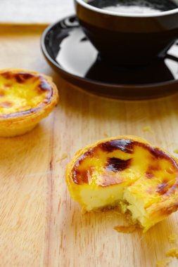 Çeyrek kesilmiş taze Portekiz yumurtalı tartlar ve arkasında bir fincan kahve.