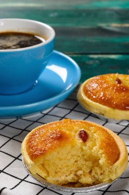 Dikey kompozisyonda bir ısırık ve bir fincan kahveyle taze horoz turtası.