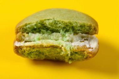 Sarı arka planda yarısı yenmiş yeşil badem kurabiyesi.