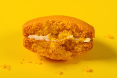 Sarı arka planda yarısı yenmiş kahverengi badem kurabiyesi.