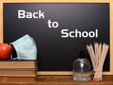 Okula geri dönen siyah tahta ve güvenlik maskesi ve yakınındaki el dezenfektanı, kaldırılabilir kelimeler, okuldaki bulaşıcı hastalık saldırısından kaçınma kavramını içeriyor