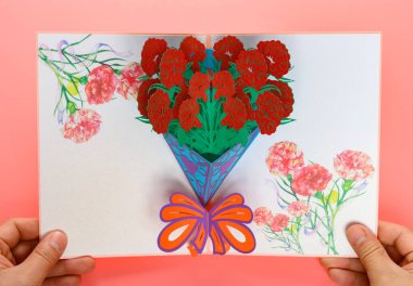 Elinde bir deste karanfil olan bir adam hediye olarak anneler günü ve kadınlar günü kartı tutuyor.