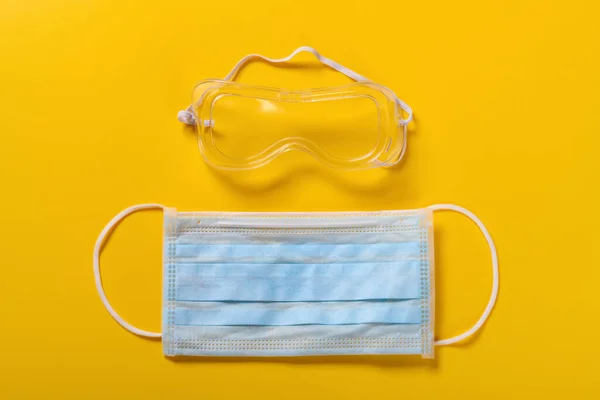 medical face mask and eye protector on yellow background