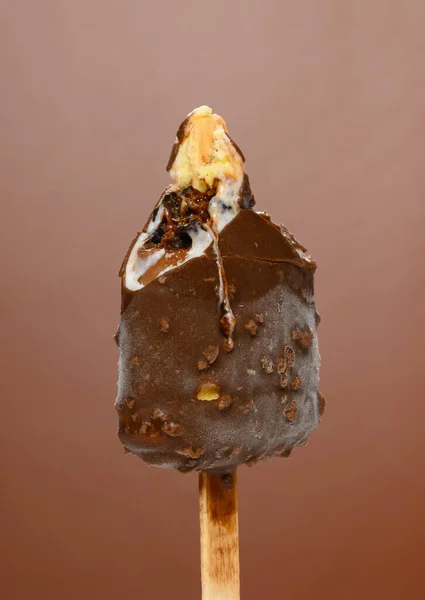 half eaten chocolate outer popsicle with blueberry sauce inside on brown background close up