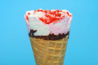 Taze vanilya ve çilekli dondurma külahı mavi arka planda.