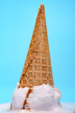 Tatlı patates aromalı dondurma külahı ters dönmüş ve mavi arka planda erimiş. Yakın plan.