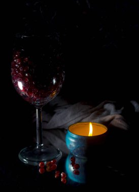 Pomegranate seeds in a glass, a lit candle in the dark.